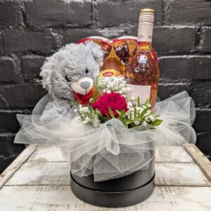 Arrangement of red roses, rosé wine, and teddy bear – angle view
