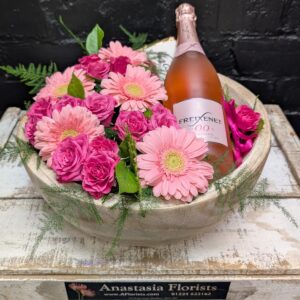 Pink flowers arranged in a wooden bowl with a bottle of sparkling drink. – close-up