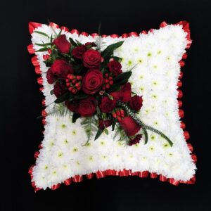 White floral cushion with red rose accent for funeral tribute