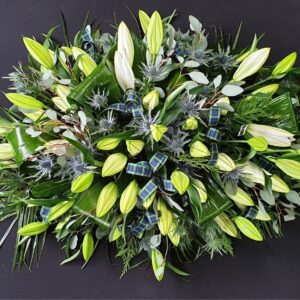 Elegant funeral coffin spray with white lilies and foliage.