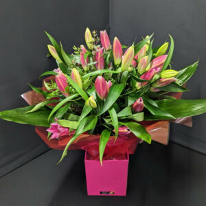 Pink lilies arranged in a bouquet with green foliage.