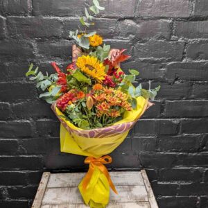 Vibrant hand-tied Autumn Glow bouquet featuring sunflowers, orange chrysanthemums, red maple leaves, and eucalyptus.