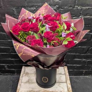 Bouquet of deep red roses and burgundy filler flowers in dark wrapping