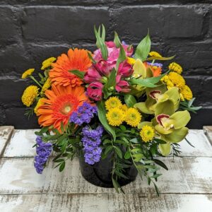 Vibrant flower arrangement in a ceramic pot featuring a mix of colorful roses, orchids, and gerbera flowers.