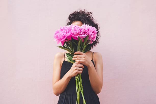 Woman holding a bouquet of pink flowers and concealing her face